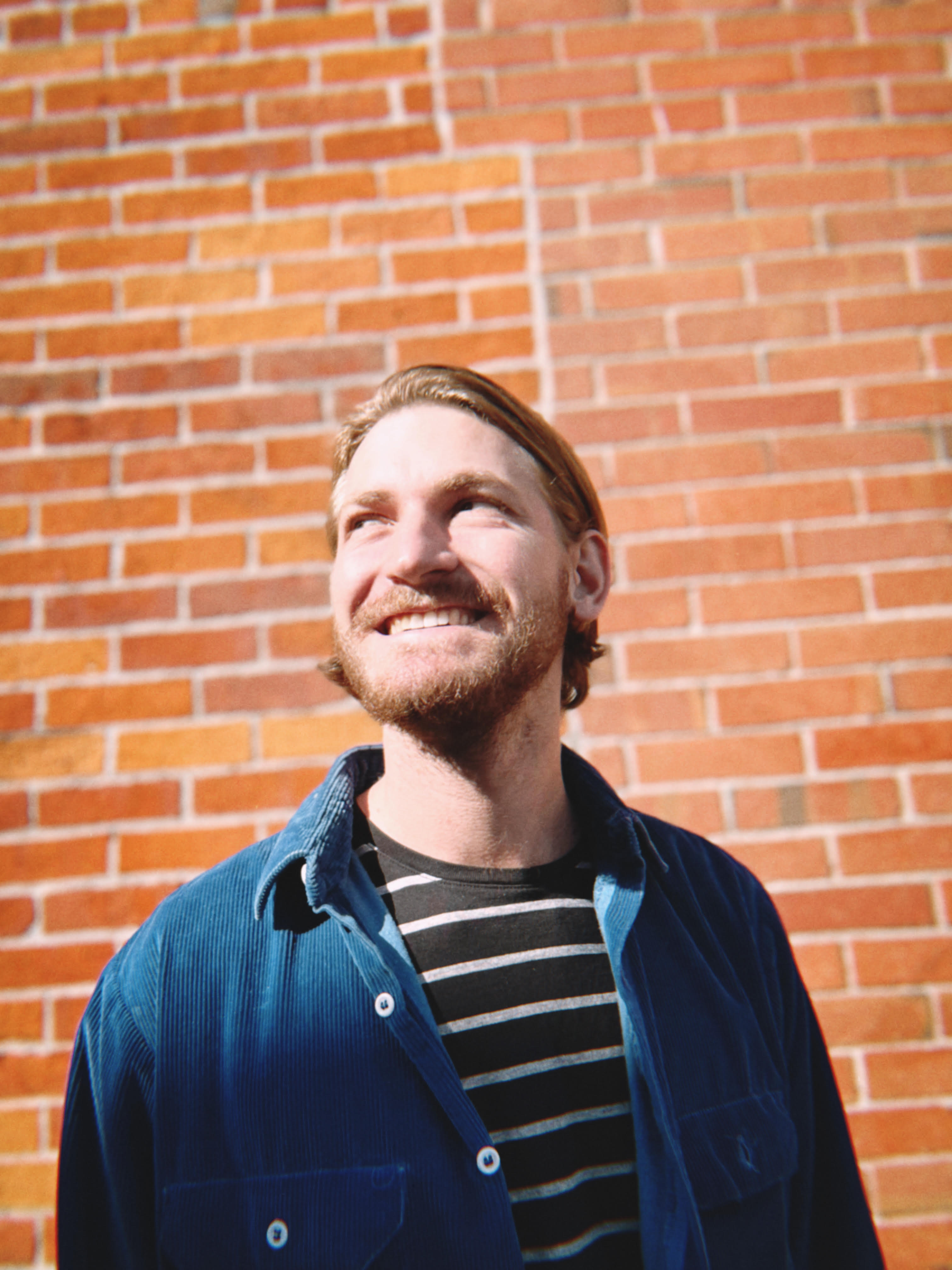 Brendan Merhab smiling in front of a brick wall